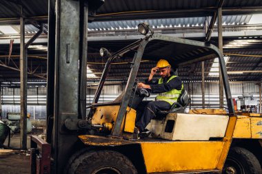 Forklift sürücüsünde çalışan adam fabrika lojistik gemisinde çalışmaktan mutlu. Depoda forklift şoförü var. Forklift sürücüsü depoda araçta oturuyor.