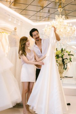 Gelin ve damat dükkanda gelinlik seçiyorlar. Gelin ve damat elbise seçip modern düğün stüdyosuna uyum sağlamaya çalışıyorlar.