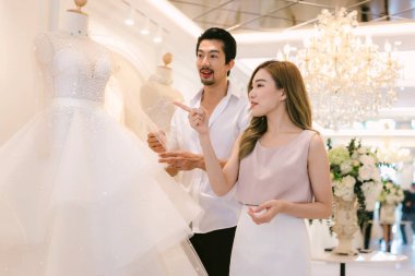 Gelin ve damat dükkanda gelinlik seçiyorlar. Gelin ve damat elbise seçip modern düğün stüdyosuna uyum sağlamaya çalışıyorlar.