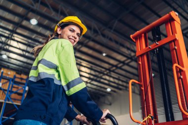 El asansörü kullanan kadın işçi endüstriyel fabrika lojistik gemisinde çalışmaktan memnun. Kadın depoda el asansörü kullanıyor. Depoda el kaldırma..