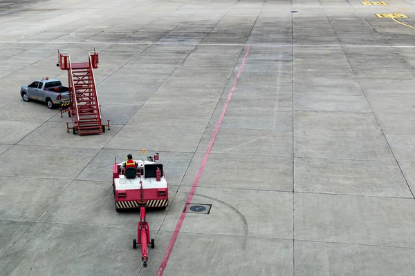 Terminalin yanındaki havaalanı önlüğündeki uçak çekici. Uçak Çekici Traktörü. Hava limanına ait çekici bir traktör subay tarafından kullanılıyor. Havaalanında traktör çekiliyor.