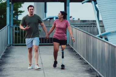 Arkadaş, dışarıda egzersiz yaparken protez bacaklı arkadaşına destek oluyor. İnsanlar parkta birlikte yürüyorlar. Yürüyüş egzersizi yapan protez bacaklı kadın ve arkadaşı parkta birlikte destek oluyor.