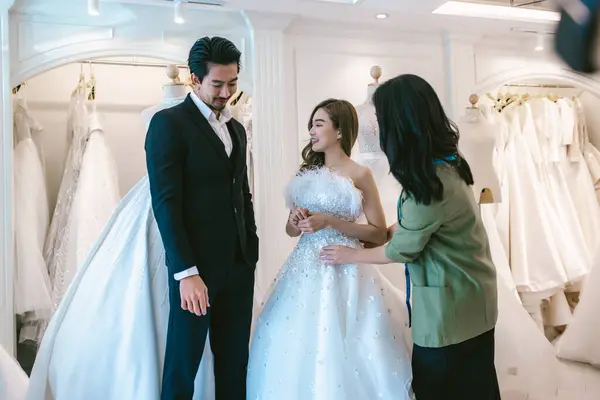 Bride and groom wear dress and try to fitting in modern wedding studio with bridal store owner