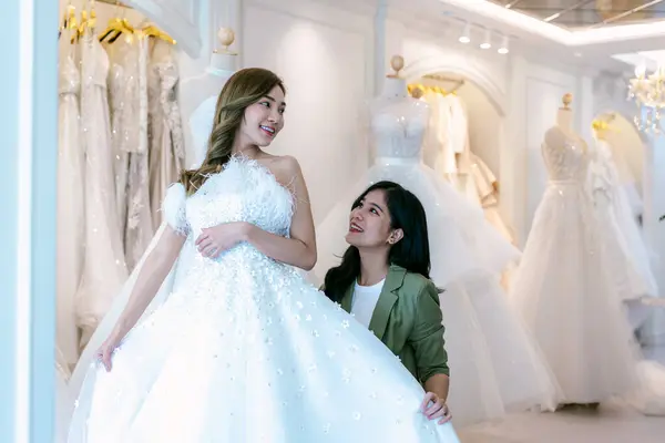 Bride and groom wear dress and try to fitting in modern wedding studio with bridal store owner