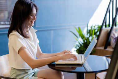 Dizüstü bilgisayarla çalışan bir kadın Coronavirus ya da Covid-19 karantinası sırasında ev işleri ile ilgileniyor. Kadın evde çalışırken dizüstü bilgisayar kullanıyor ve gülümsüyor.