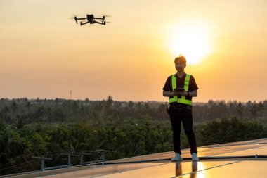 Teknoloji güneş pili mühendisliği, fabrikanın çatısındaki güneş pilini kontrol ediyor. Mühendis kontrol dronu, güneş enerjili çatı panelinin fabrikanın çatısına gün batımının altında kurulumunu kontrol ediyor. 