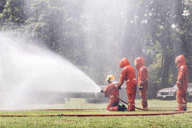 İtfaiyeci konsepti. Birkaç itfaiyeci bir yangın saldırısı için saldırıya geçiyor. İtfaiyeci ateş aleviyle savaşmak için su ve yangın söndürücü kullanıyor.. 
