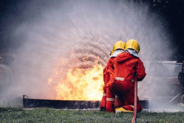 İtfaiyeci konsepti. Birkaç itfaiyeci bir yangın saldırısı için saldırıya geçiyor. İtfaiyeci ateş aleviyle savaşmak için su ve yangın söndürücü kullanıyor.. 