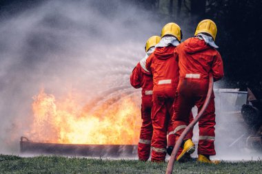 İtfaiyeci konsepti. Birkaç itfaiyeci bir yangın saldırısı için saldırıya geçiyor. İtfaiyeci ateş aleviyle savaşmak için su ve yangın söndürücü kullanıyor.. 