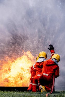 İtfaiyeci konsepti. Birkaç itfaiyeci bir yangın saldırısı için saldırıya geçiyor. İtfaiyeci ateş aleviyle savaşmak için su ve yangın söndürücü kullanıyor.. 