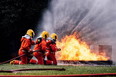 İtfaiyeci konsepti. Birkaç itfaiyeci bir yangın saldırısı için saldırıya geçiyor. İtfaiyeci ateş aleviyle savaşmak için su ve yangın söndürücü kullanıyor.. 