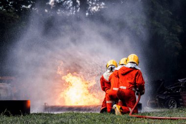 İtfaiyeci konsepti. Birkaç itfaiyeci bir yangın saldırısı için saldırıya geçiyor. İtfaiyeci ateş aleviyle savaşmak için su ve yangın söndürücü kullanıyor.. 