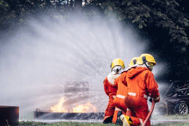 İtfaiyeci konsepti. Birkaç itfaiyeci bir yangın saldırısı için saldırıya geçiyor. İtfaiyeci ateş aleviyle savaşmak için su ve yangın söndürücü kullanıyor.. 