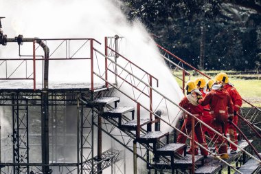 İtfaiyeci konsepti. Birkaç itfaiyeci bir yangın saldırısı için saldırıya geçiyor. İtfaiyeci ateş aleviyle savaşmak için su ve yangın söndürücü kullanıyor.. 