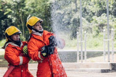 İtfaiyeci konsepti. Birkaç itfaiyeci bir yangın saldırısı için saldırıya geçiyor. İtfaiyeci ateş aleviyle savaşmak için su ve yangın söndürücü kullanıyor.. 