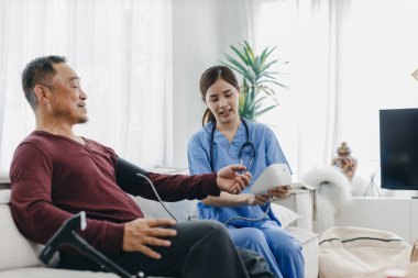 Caregiver nurse measuring blood pressure by using digital sphygmomanometer Senior patient at home. Caregiver nurse using medical device to measure blood pressure Senior patient.	