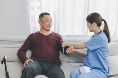 Caregiver nurse measuring blood pressure by using digital sphygmomanometer Senior patient at home. Caregiver nurse using medical device to measure blood pressure Senior patient.	