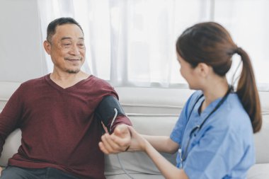 Caregiver nurse measuring blood pressure by using digital sphygmomanometer Senior patient at home. Caregiver nurse using medical device to measure blood pressure Senior patient.	