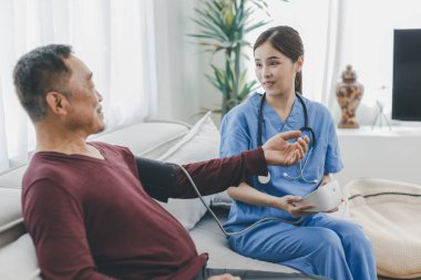Caregiver nurse measuring blood pressure by using digital sphygmomanometer Senior patient at home. Caregiver nurse using medical device to measure blood pressure Senior patient.	