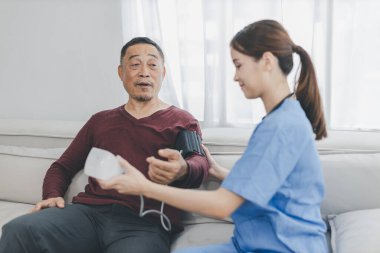 Caregiver nurse measuring blood pressure by using digital sphygmomanometer Senior patient at home. Caregiver nurse using medical device to measure blood pressure Senior patient.	