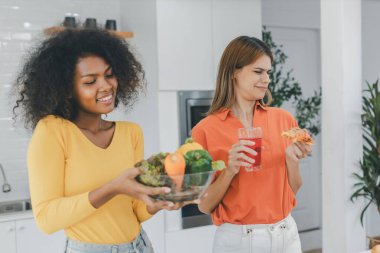 Sebze ve sosis, organik gıda ve GMO ürünleri arasında seçim yapan iki kadın. Mutfakta sağlıklı yiyecekler yemeyi seçen genç bir kadın abur cubur, şişman ve sağlıksız yemekleri karşılaştırıyor. 