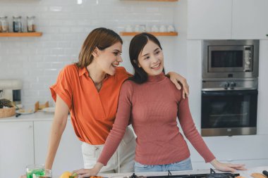 Mutfak odasında kucaklaşan çok ırklı lezbiyen çift. Yüzük tutan siyah beyaz bir çift. Afro-Amerikan ve beyaz lezbiyen çift birbirlerine şefkatle sarılıp bakıyorlar.