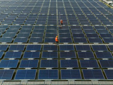 Göl üzerinde yüzen güneş panelleri ya da güneş pili platformu sistemini fırça ve suyla temizleyen işçiler. Bir güneş enerjisi santralinde güneş modüllerini temizleyen işçiler