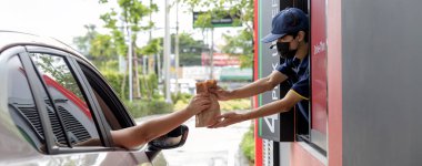 El Adam, fast food restoranından kahve alıyor. Teslimat penceresinde servis servisi yapan personel. Buradan geç ve hazır yemek al. Covid19 'u koru..