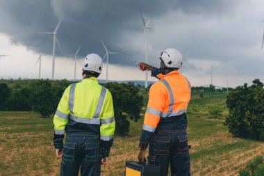 Mühendis, fırtına sırasında arka planda yağmur bulutları olan bir rüzgar türbininin bakım görüntüsünü kontrol ediyor. Bulutlu bir günde rüzgar türbininde çalışan mühendis. 