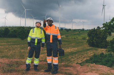 Mühendis, fırtına sırasında arka planda yağmur bulutları olan bir rüzgar türbininin bakım görüntüsünü kontrol ediyor. Bulutlu bir günde rüzgar türbininde çalışan mühendis. 