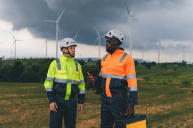 Mühendis, fırtına sırasında arka planda yağmur bulutları olan bir rüzgar türbininin bakım görüntüsünü kontrol ediyor. Bulutlu bir günde rüzgar türbininde çalışan mühendis. 