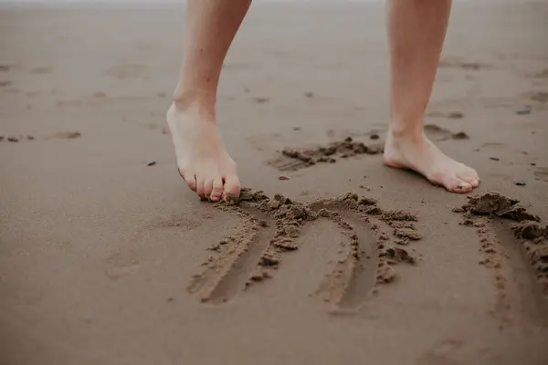 Drawing on the sand with your feet. Women's legs. Exercise against flat feet. Foot health.Clean sand. Inscriptions on the sand
