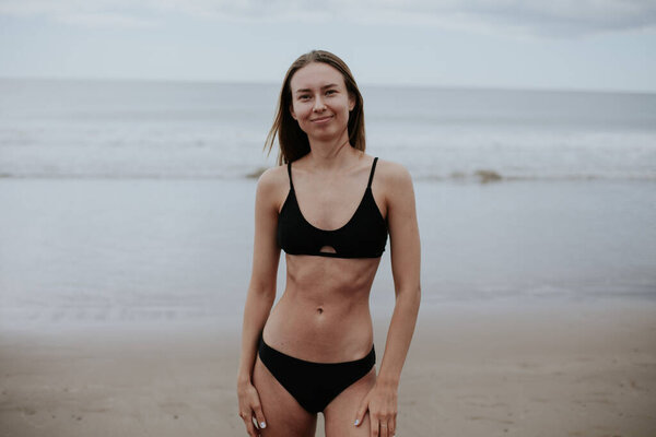 Beautiful ukrainian woman in black bikini on tropical beach. Portrait of happy young woman smiling at sea. Brunette tanned girl in swimwear enjoying and walking on beach.