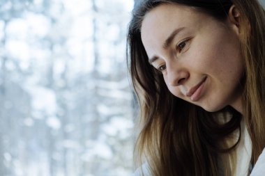 Bir kadının portre fotoğrafı. Bakışlar aşağıya bakıyor. Pencereden ormanın manzarası.