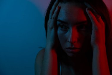 Duygusal bir fotoğraf. Mavi ve kırmızı renkler. Bir kadının portre fotoğrafı. Genç bir kadın kendini stresli ve endişeli hisseder. Bir kadın karanlıkta yalnız başına sızlanır. Depresyonda olan genç bir kadın kayıplarıyla, kederiyle baş eder.