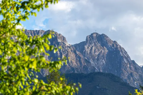 Tatra Dağları ve Giewont Zirvesi manzarası. Yeşil çayır, yol dağların yamacına çıkıyor. Yolun yanında ağaçlar var. Tatra Dağlarında yaz