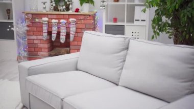 Noel çorapları ve Noel ağacı ışıklarıyla süslenmiş şömine. Noel süslemelerinin arka planında gri kanepe.