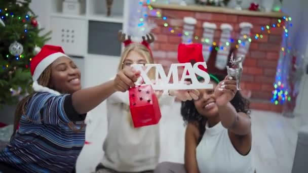 Meisjes Houden Kerstsymbolen Hand Kerstinscriptie Lachende Afrikaanse Europese Vrouwen Zitten — Stockvideo