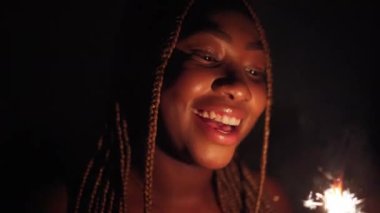 Neşe dolu esmer tenli bir kız yanan soğuk ateşi seyrediyor ve gülümsüyor. Yeni yıl arifesi ve yeni yıl arifesi boyunca kutlama.