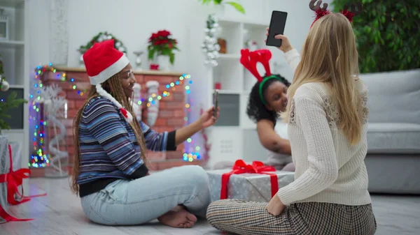 Selfie during a Christmas gathering. Two African and one European women sit on the floor in a Turkish style. A gift with a red bow.