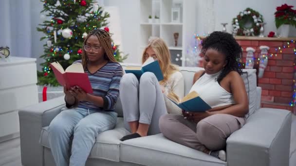 女孩们在书中寻找有趣的故事 并把它们展示给她们的朋友 姑娘们笑了圣诞节 一个非洲女人和一个欧洲女人在一起 — 图库视频影像