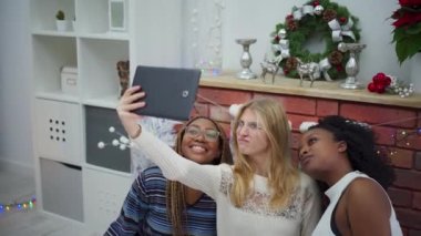 Farklı kıtalardan gülümseyen arkadaşlar şöminenin önünde selfie çekiyorlar. Uluslararası Noel.