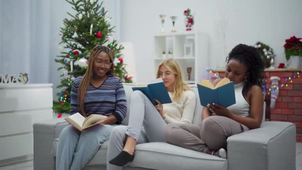客厅里 两个非洲女人和一个欧洲女人坐在沙发上看书 为圣诞节装饰的客厅 — 图库视频影像