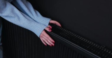 Kız sıcak bir radyatöre dokunarak donmuş ellerini ısıtıyor. Kışın merkezi ısıtmayı çalıştırmak gereklidir..