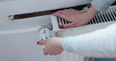 Para biriktirmek için, kız radyatörün ısısını elle düşürüyor. Evde ısı enerjisinin sorumlu kullanımı.