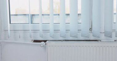 Dikey jaluziler takarak pencereyi dekore et. Dikey perdeler radyatörden gelen sıcak havanın etkisiyle yavaşça dalgalanıyor..