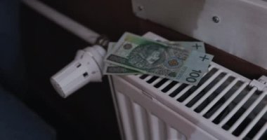 Bir kadının eli, banknotları radyatörün üstüne koyar. Büyük miktarlarda banknotlar. Her evde ısıtma enerjisi zammı.