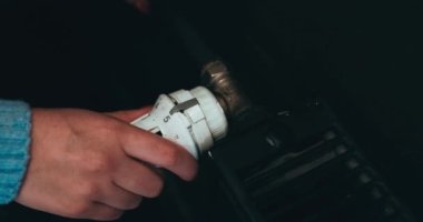 Radyatörün ısısını vidalıyorum. Radyatör sıcaklık düğmesini ayarlıyorum. Bir kadının eli merkezi ısıtma sisteminin sıcaklığını değiştirir..