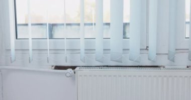 Dikey jaluziler takarak pencereyi dekore et. Dikey perdeler radyatörden gelen sıcak havanın etkisiyle yavaşça dalgalanıyor..