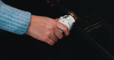 Radyatörün ısısını vidalıyorum. Radyatör sıcaklık düğmesini ayarlıyorum. Bir kadının eli merkezi ısıtma sisteminin sıcaklığını değiştirir..